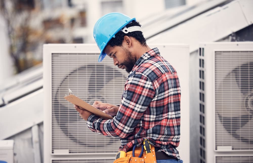 Man stood next to heat pump, looking at a clipboard