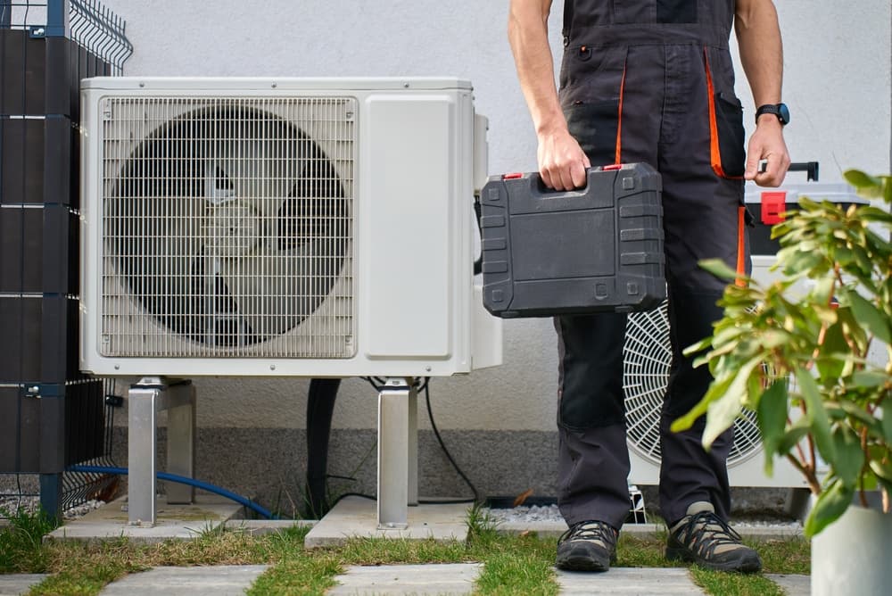 Installer with a toolbox standing next to a heat pump 